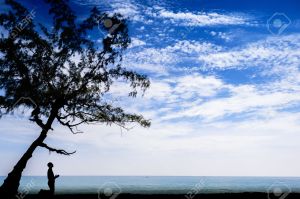 Man Praying Under a Tree in Silhouette by the beach and blue sky